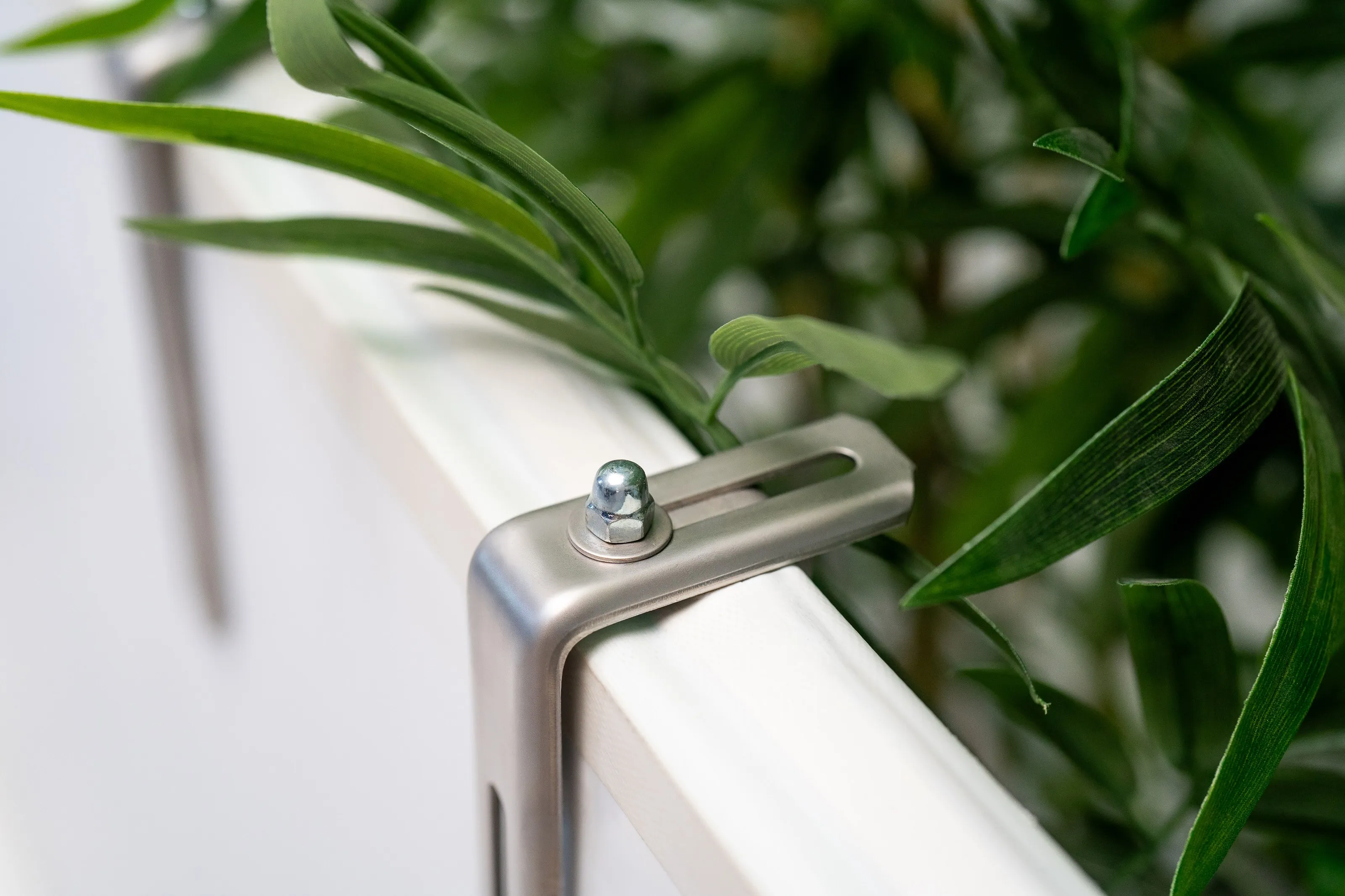 Suport pentru jardinieră din oțel inoxidabil pe o balustradă plată albă printre plante verzi
