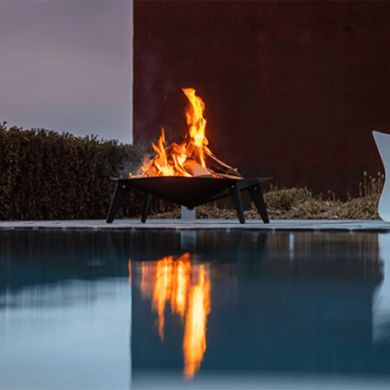 Braciere ALBA con fuoco acceso a bordo piscina al crepuscolo